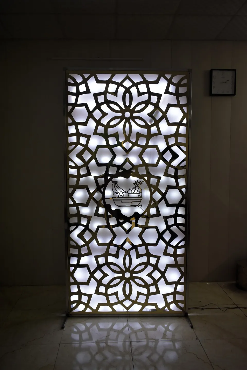 Backlit laser-cut screen in gold-tone PVD stainless steel with a floral pattern